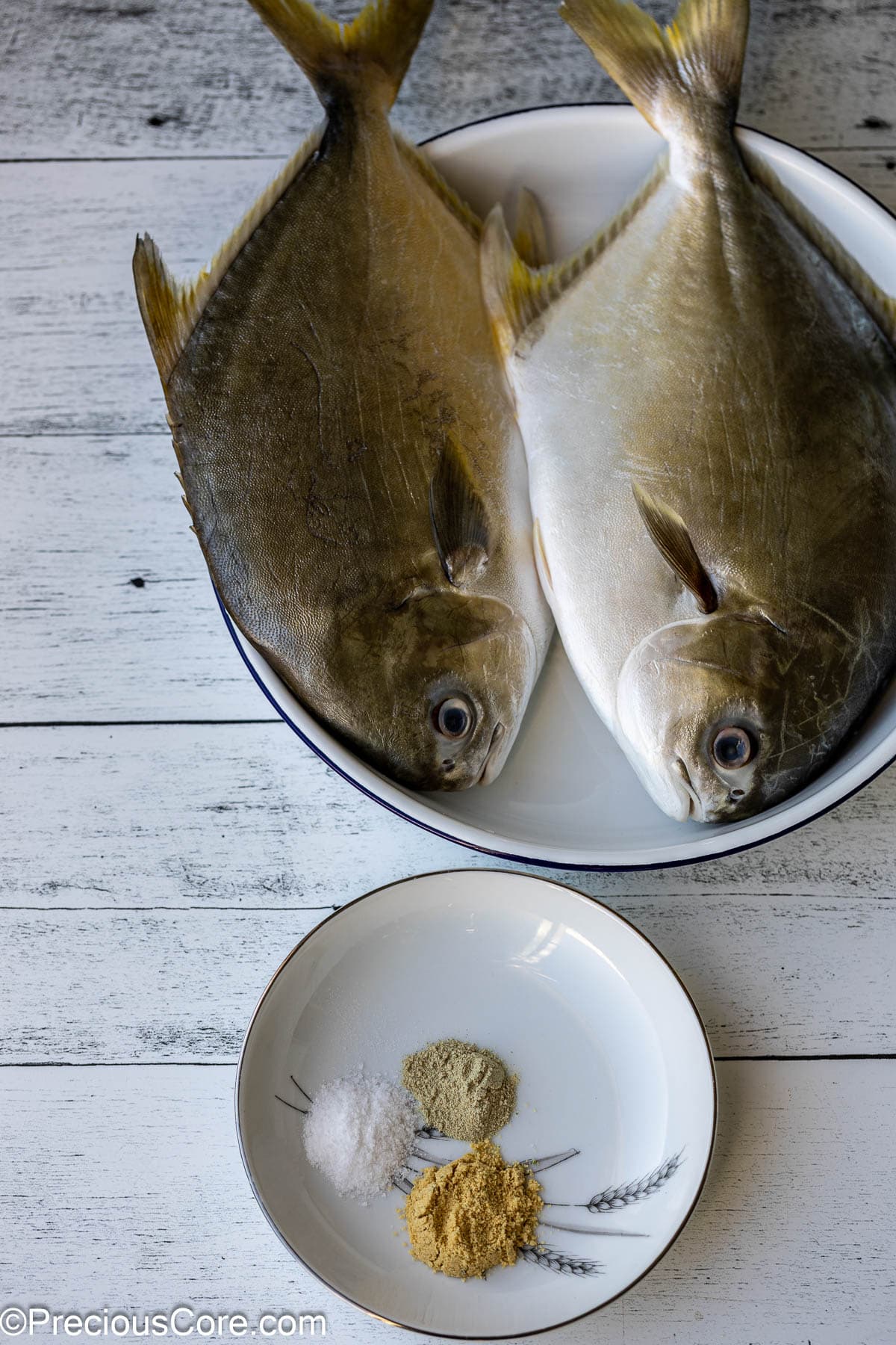 2 whole fish in a white bowl, a small plate with seasoning.