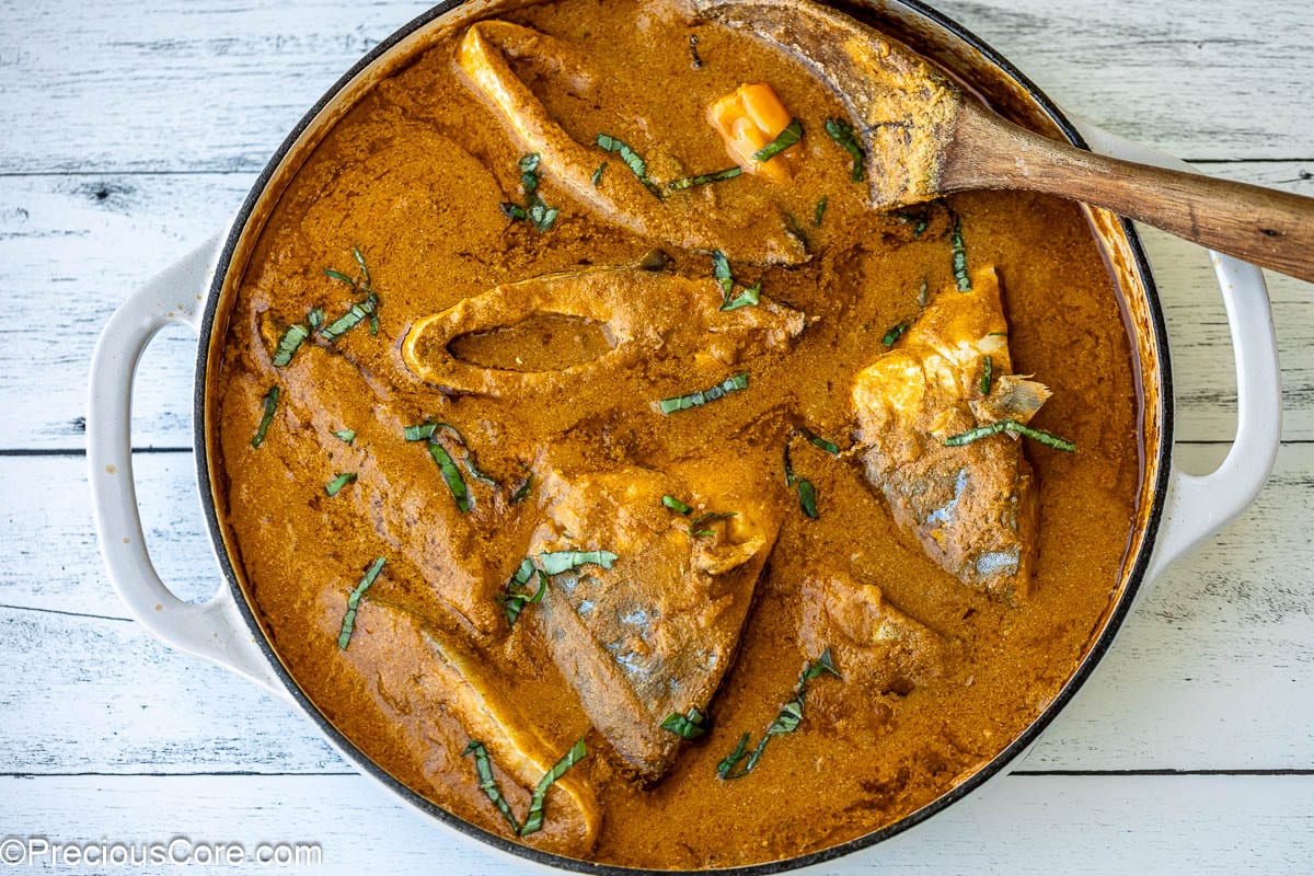 A white pot filled with stew and fish steaks.