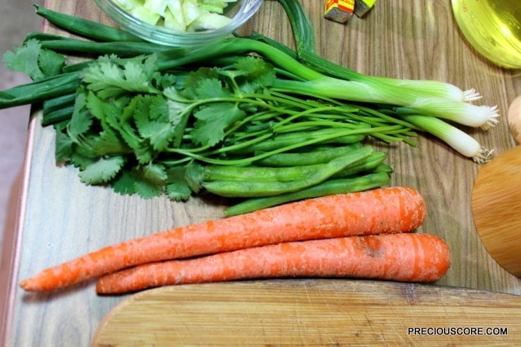 Carrots, green beans, and other produce on a wooden cutting board.
