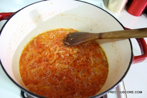 Wooden spoon stirring a pan with tomatoes.