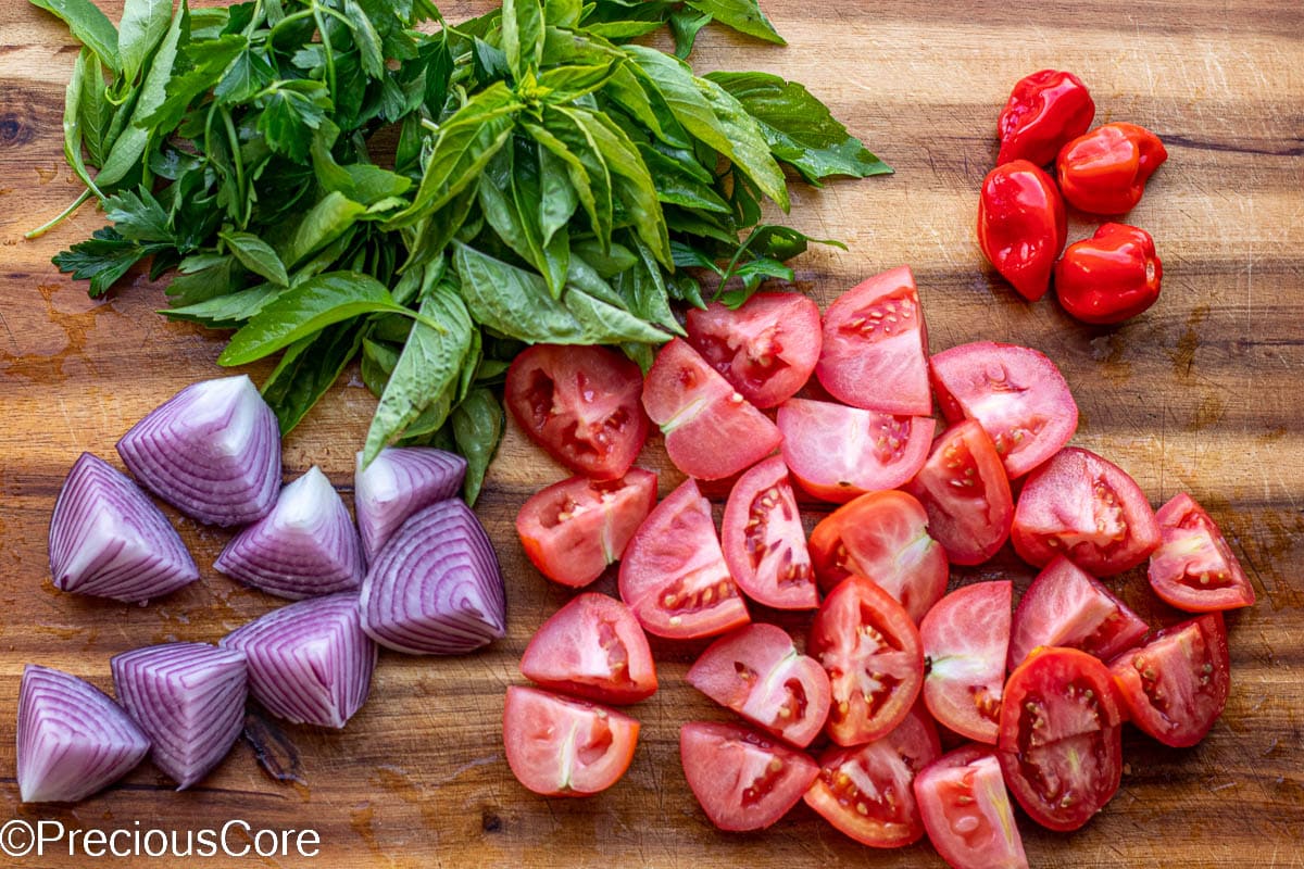 Tomatoes, habanero peppers, onions, and herbs on a cutting board.