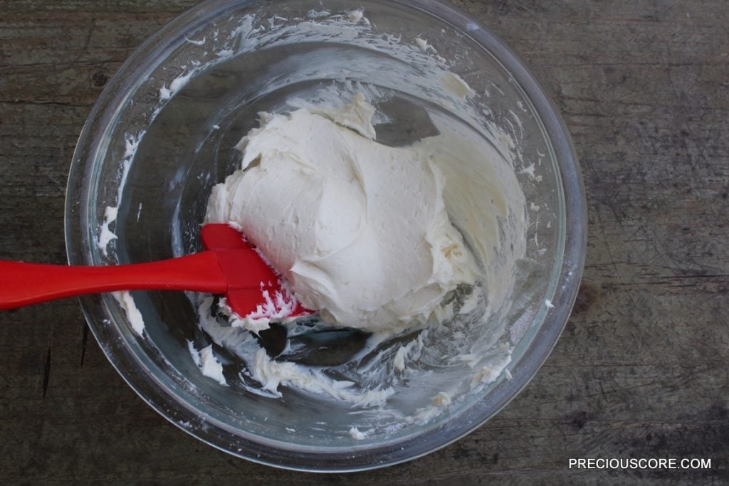 Red spatula mixing cream cheese filling ingredients.
