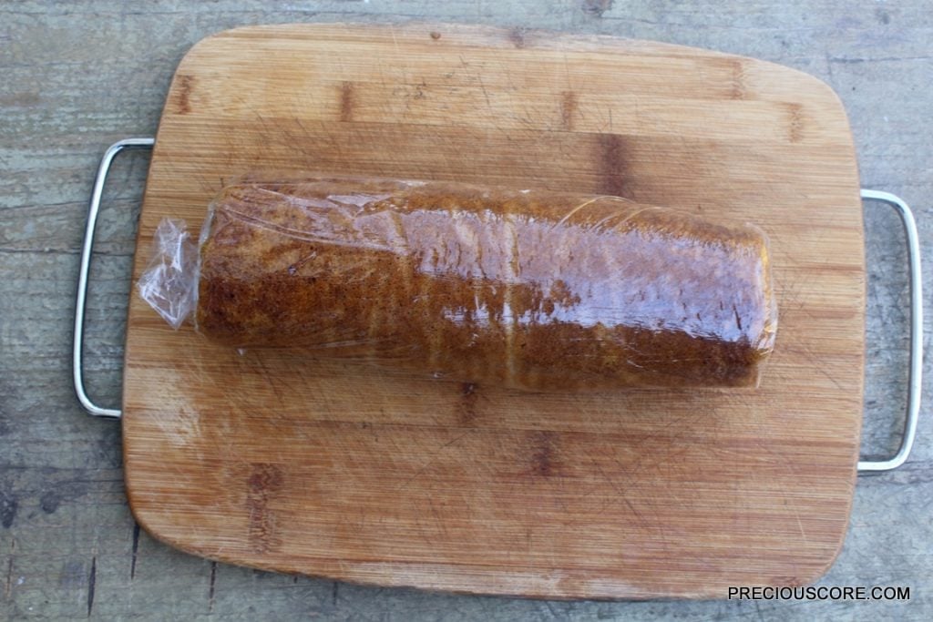 Pumpkin cake and cream cheese filling rolled together on a wooden cutting board.