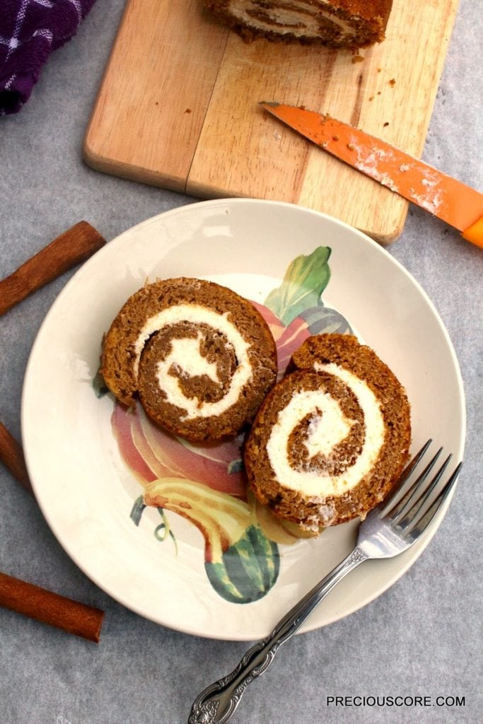 Two slices of pumpkin roll cake on a decorated plate with a fork.