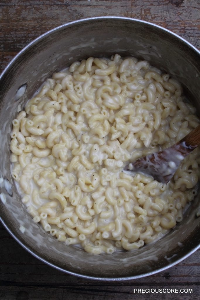 Wooden spoon stirring a pot of macaroni and cheese.