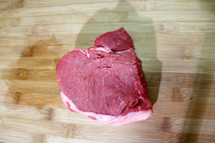 Piece of top sirloin steak on a wooden cutting board.