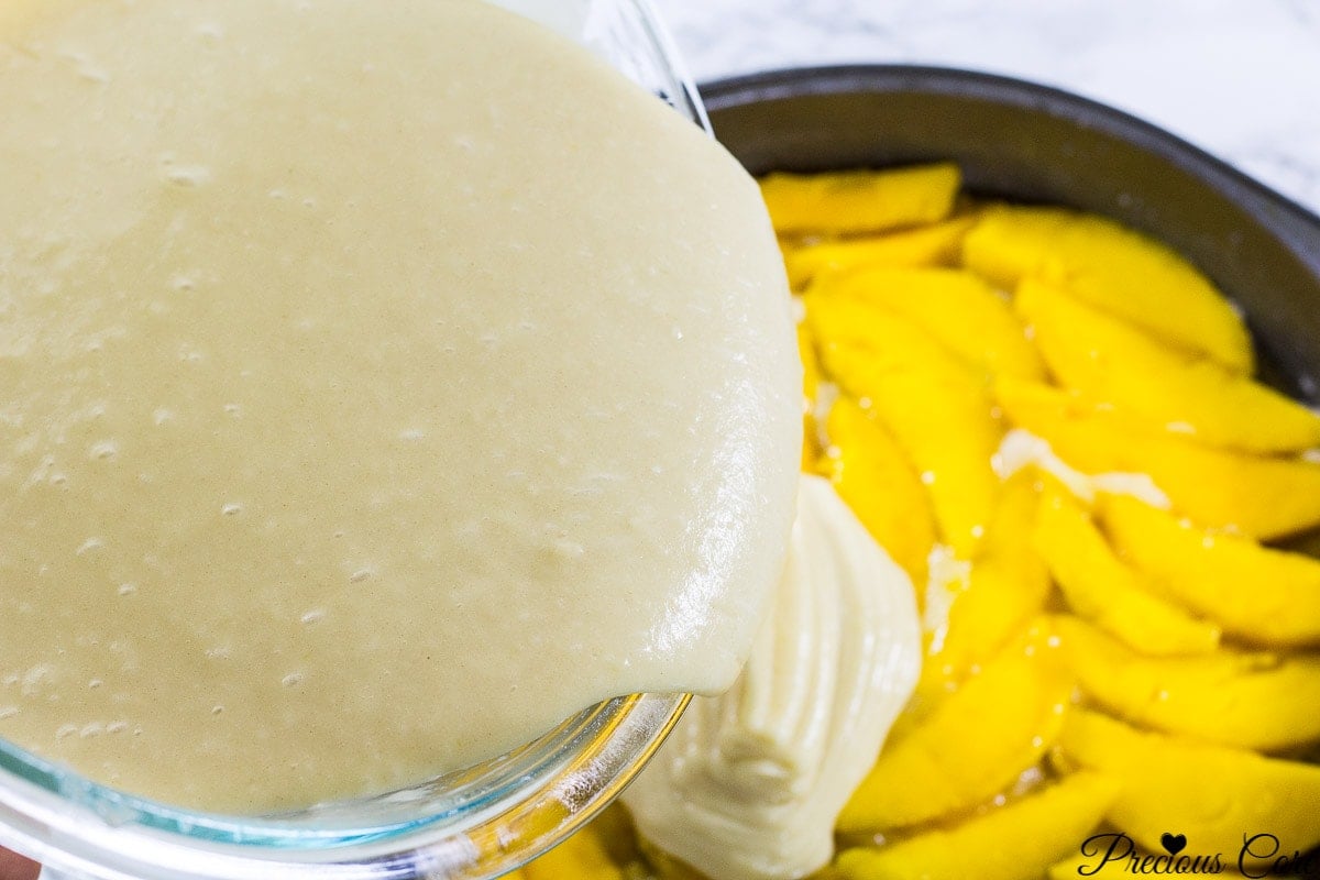 Cake batter pouring over sliced mangos.