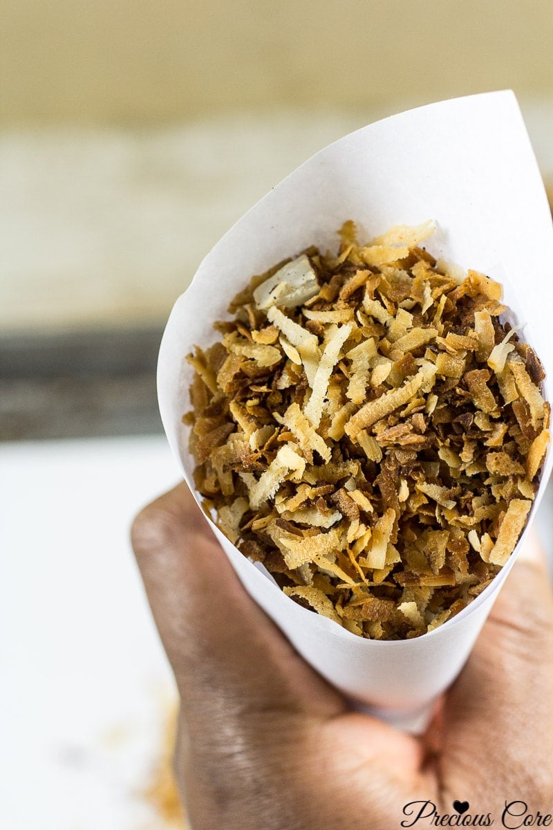 Person holding a paper cone of toasted coconut flakes.