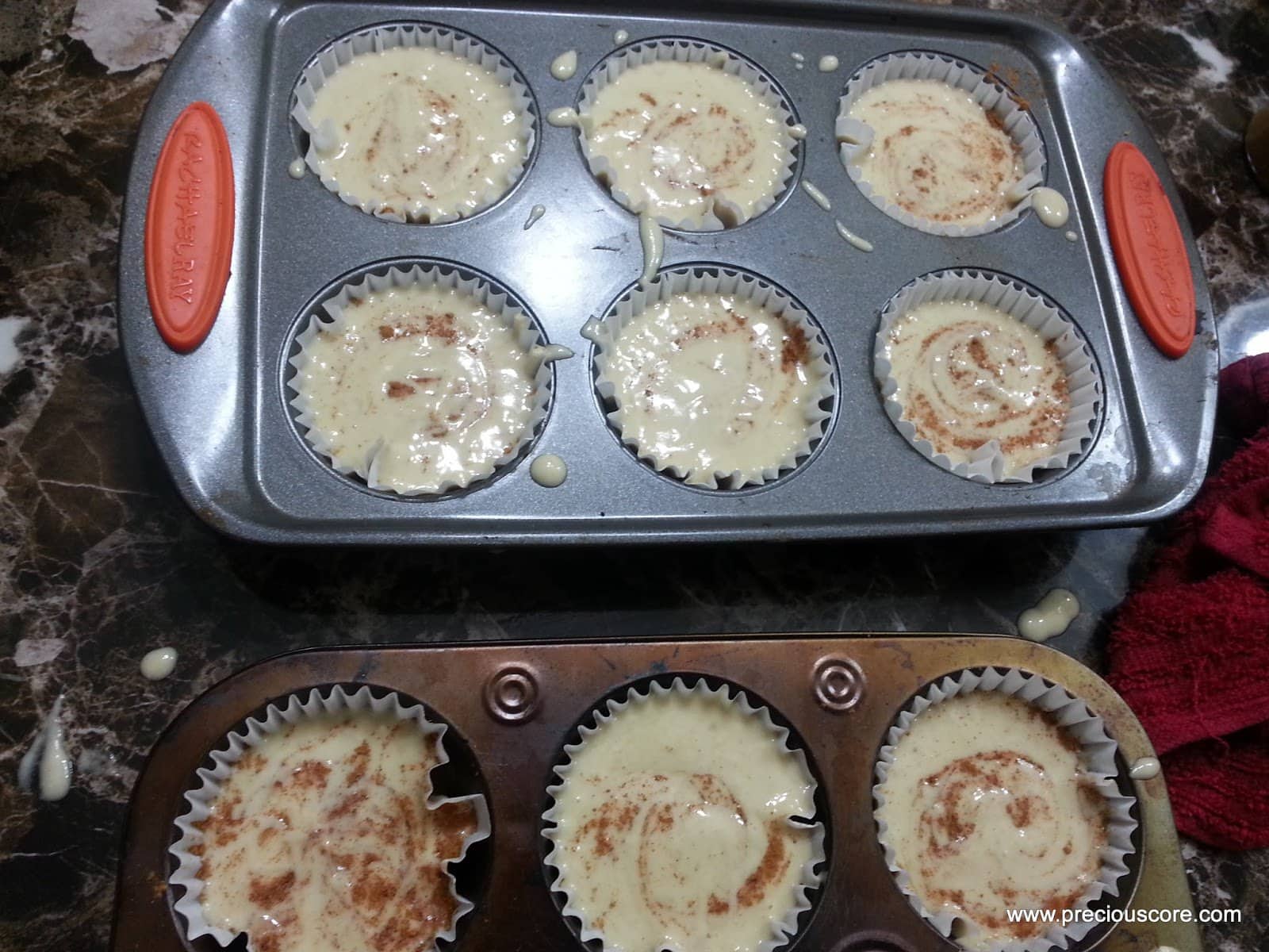 Muffin pan full of banana cake batter swirled with cinnamon.