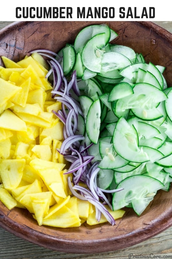 Bowl of unmixed salad with text \"Cucumber Mango Salad.\"