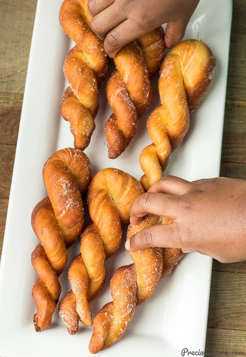 Hand grabbing a twisted African doughnut from a platter of doughnuts.
