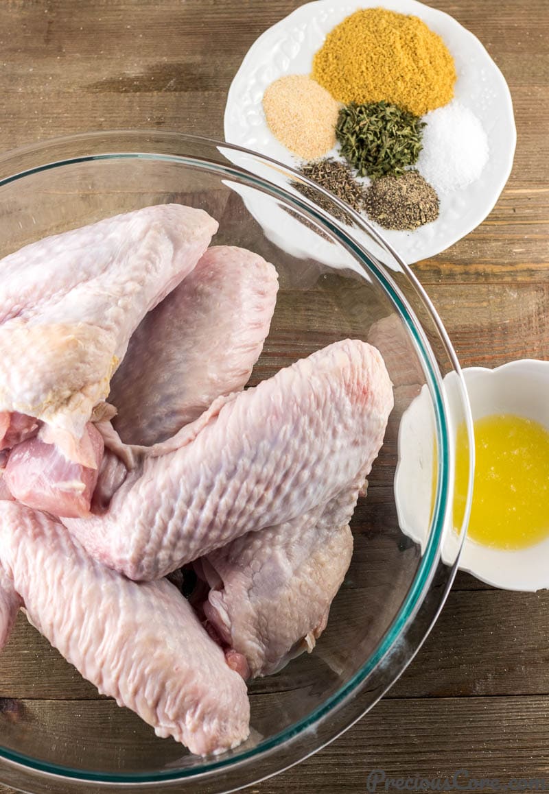 Fresh turkey wings in a bowl, spices and herbs on a plate, and melted butter in a small bowl.