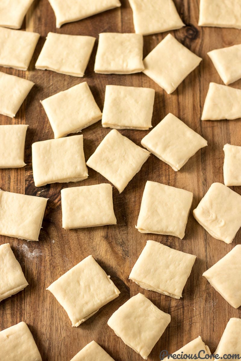 Beignet dough squares on a wooden surface.