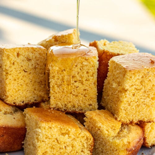 Square slices of cornbread without buttermilk with honey drizzling on top.