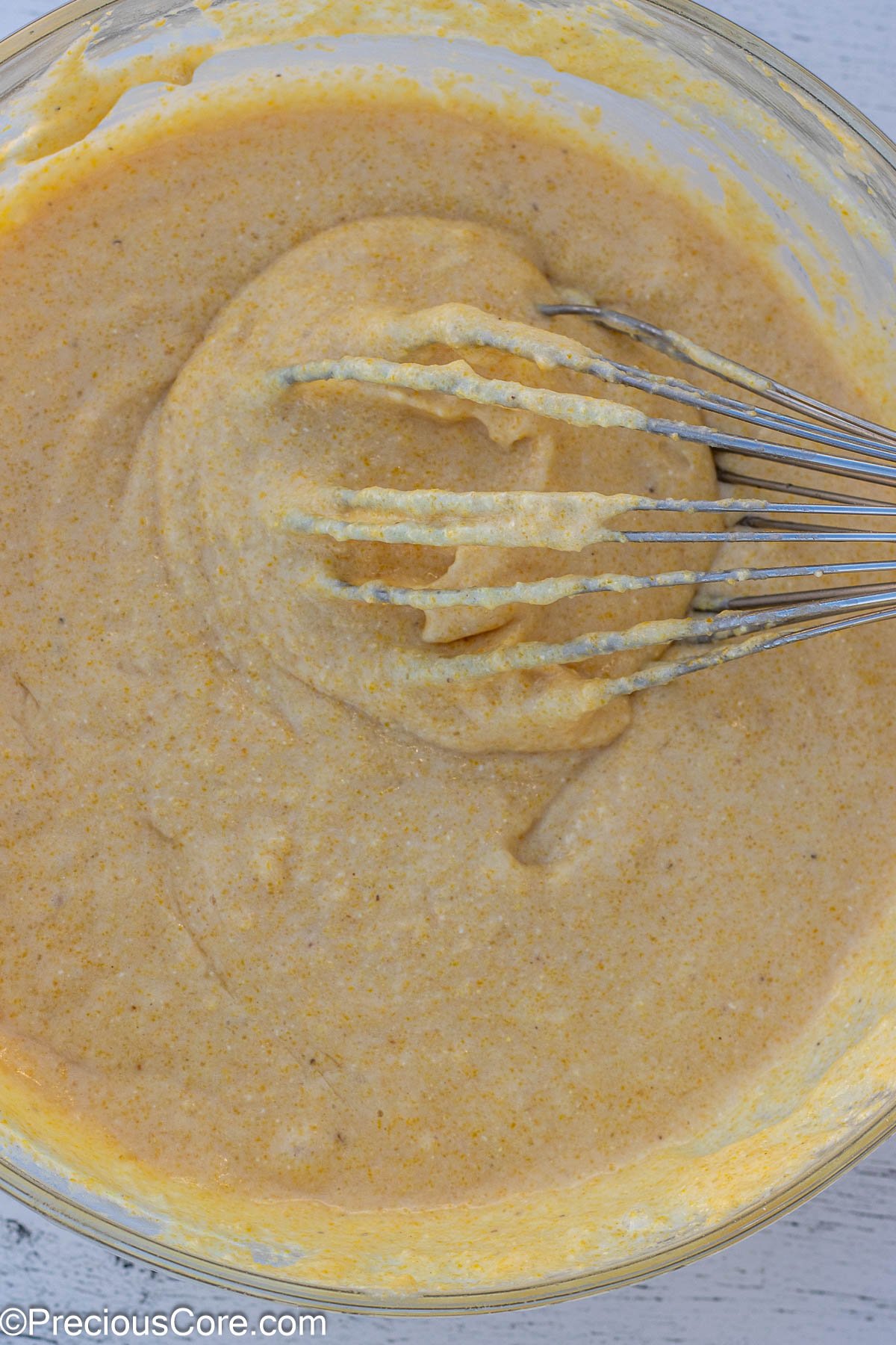 Batter for cornbread with a whisk in a bowl.