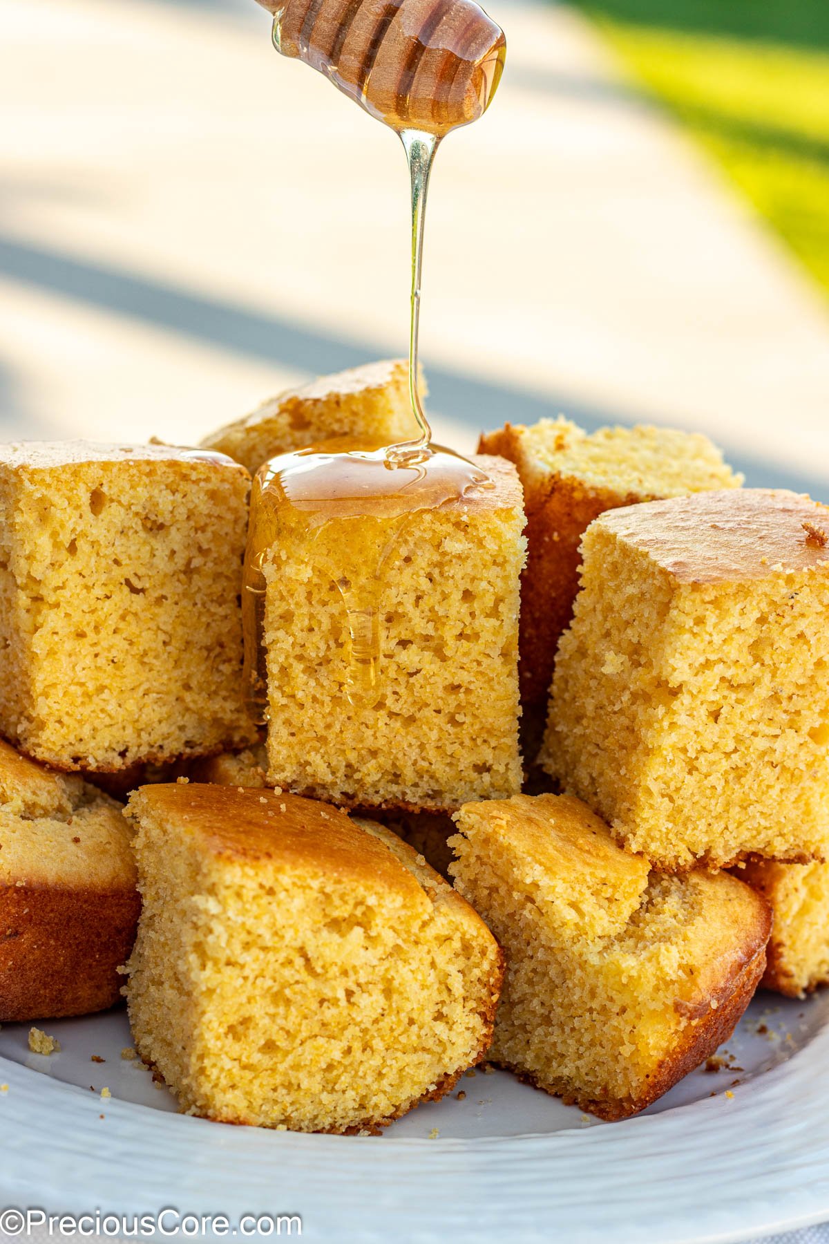 Square slices of cornbread without buttermilk with honey drizzling on top.