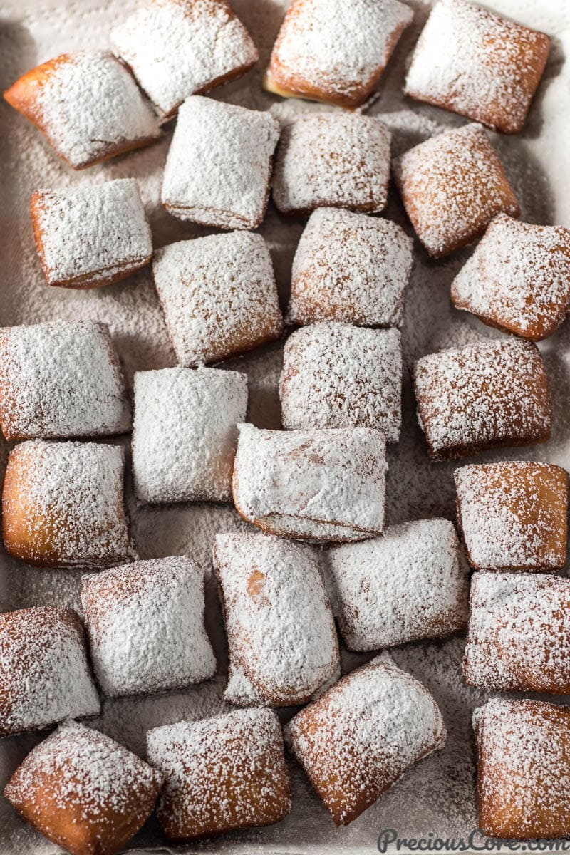 Cooked Beignets covered with powdered sugar on a lined baking sheet.