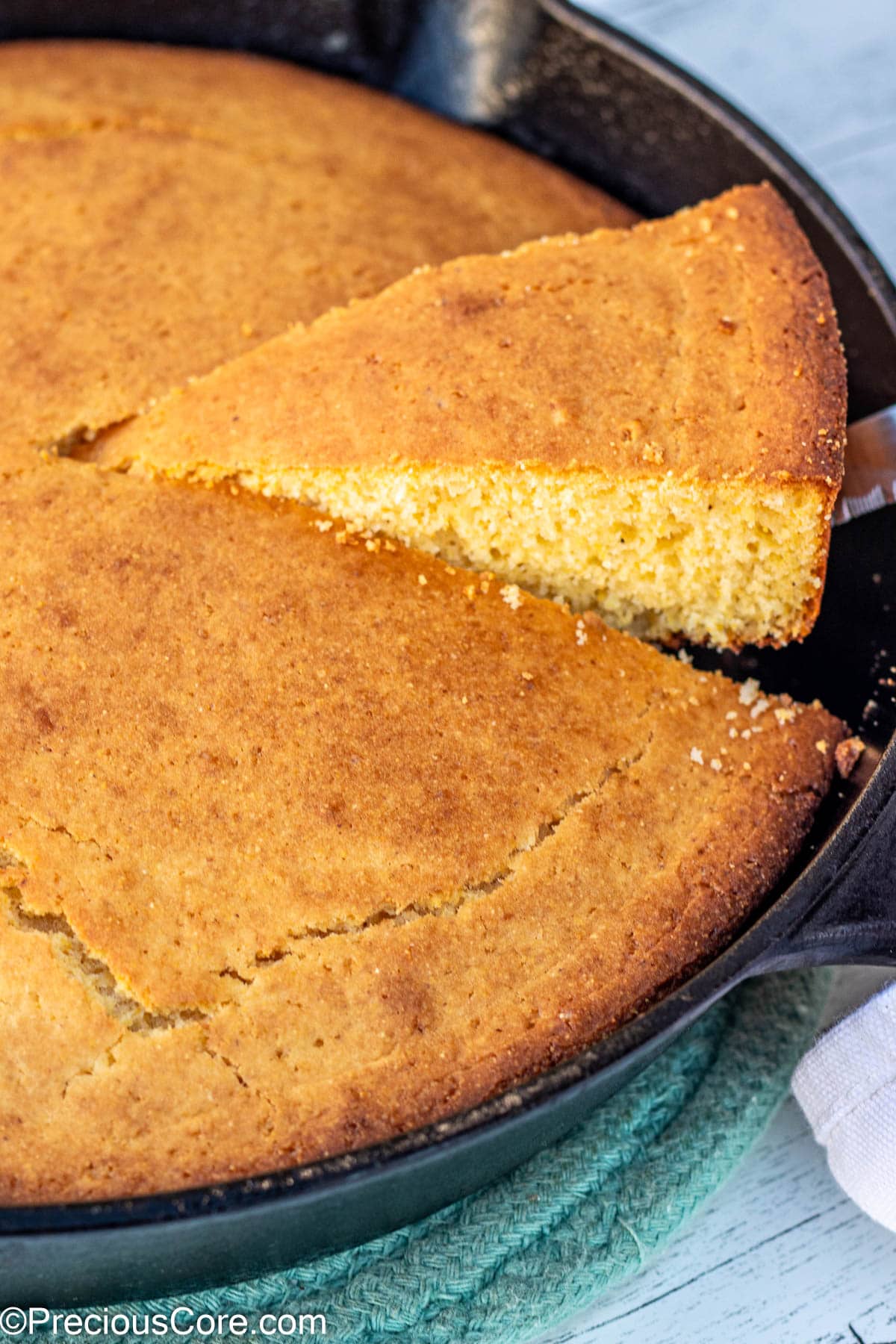 Slice of cornbread being lifted from a cast iron skillet.