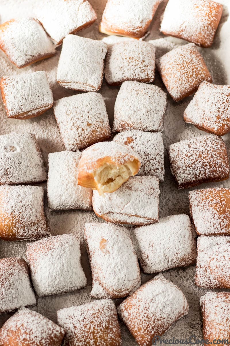 Tray of beignets, one of which is missing a bite.