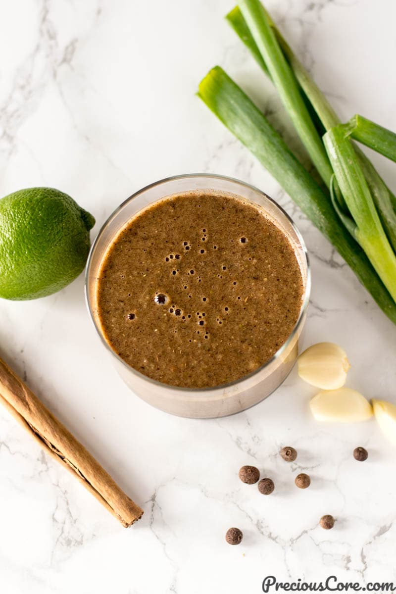 Glass of Jamaican jerk seasoning surrounded by ingredients such as garlic and lime.