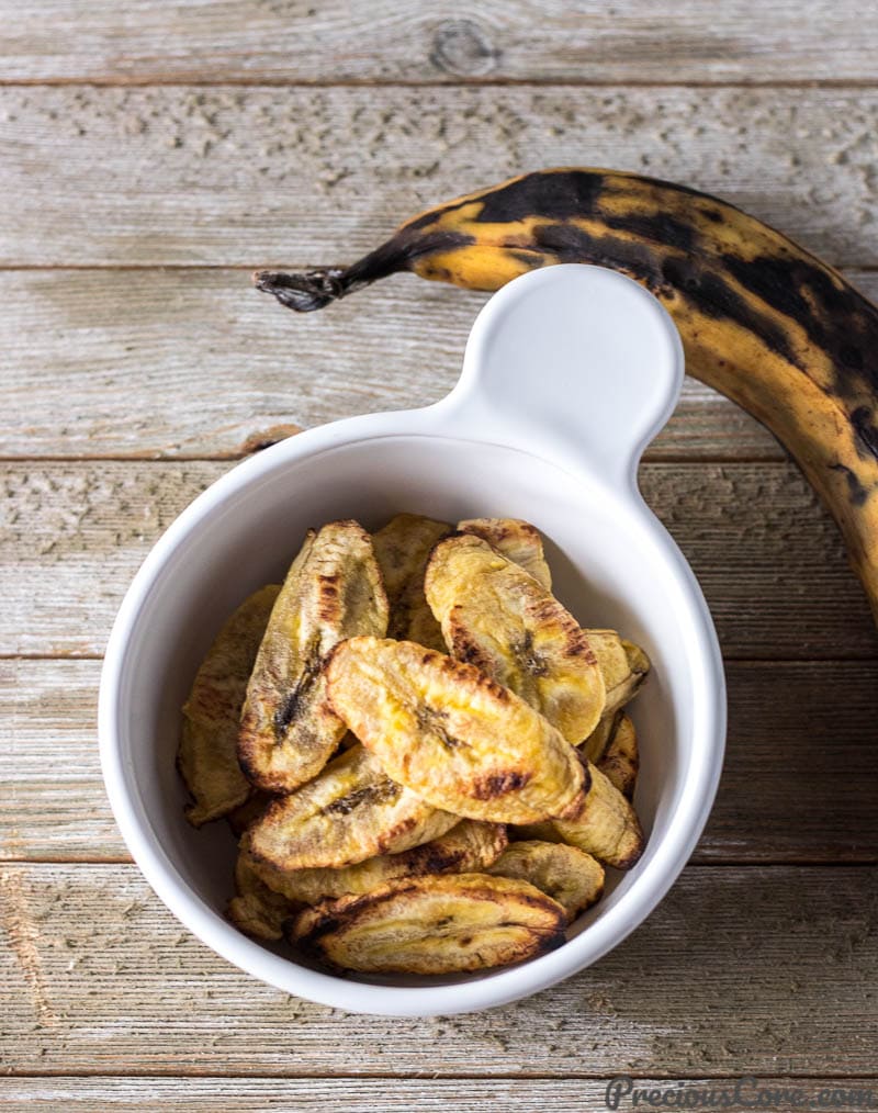 Baked Plantains in a bowl but one whole uncooked ripe plantain on the side