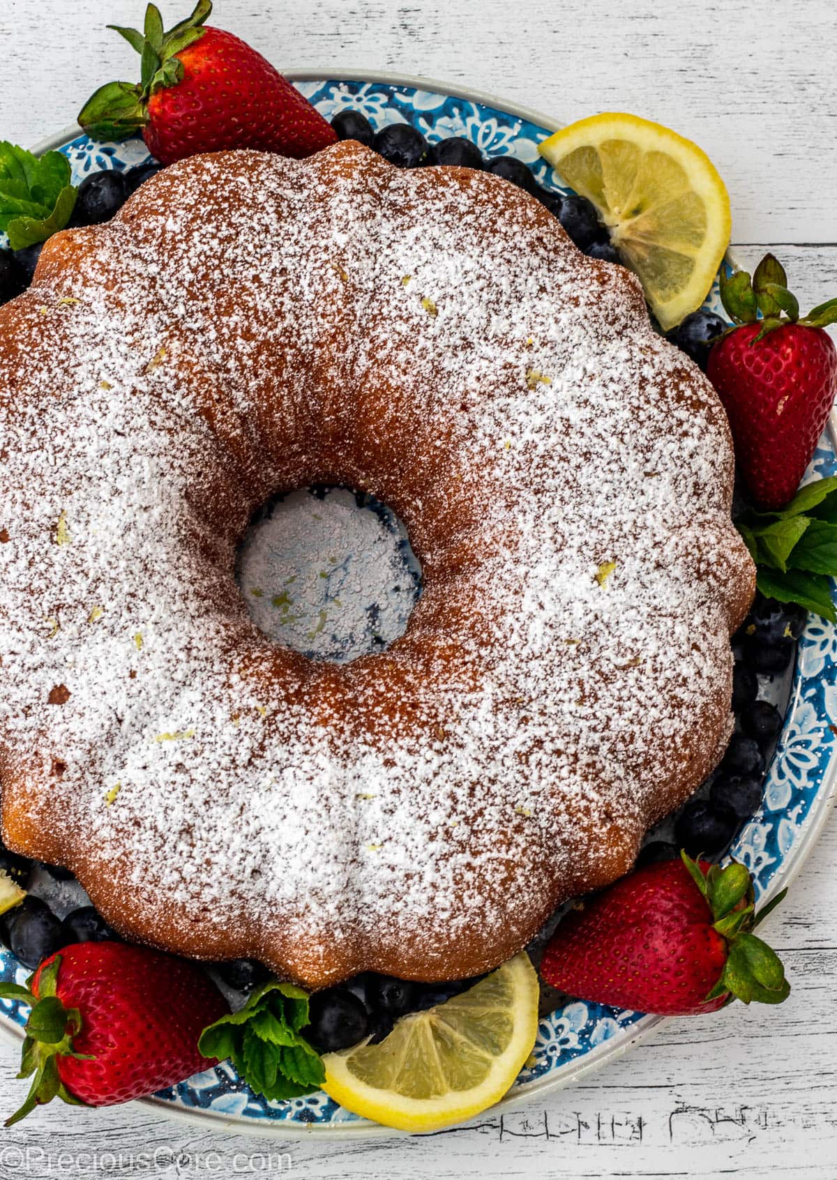 A bundt cake dusted with powdered sugar and surrounded by berries.