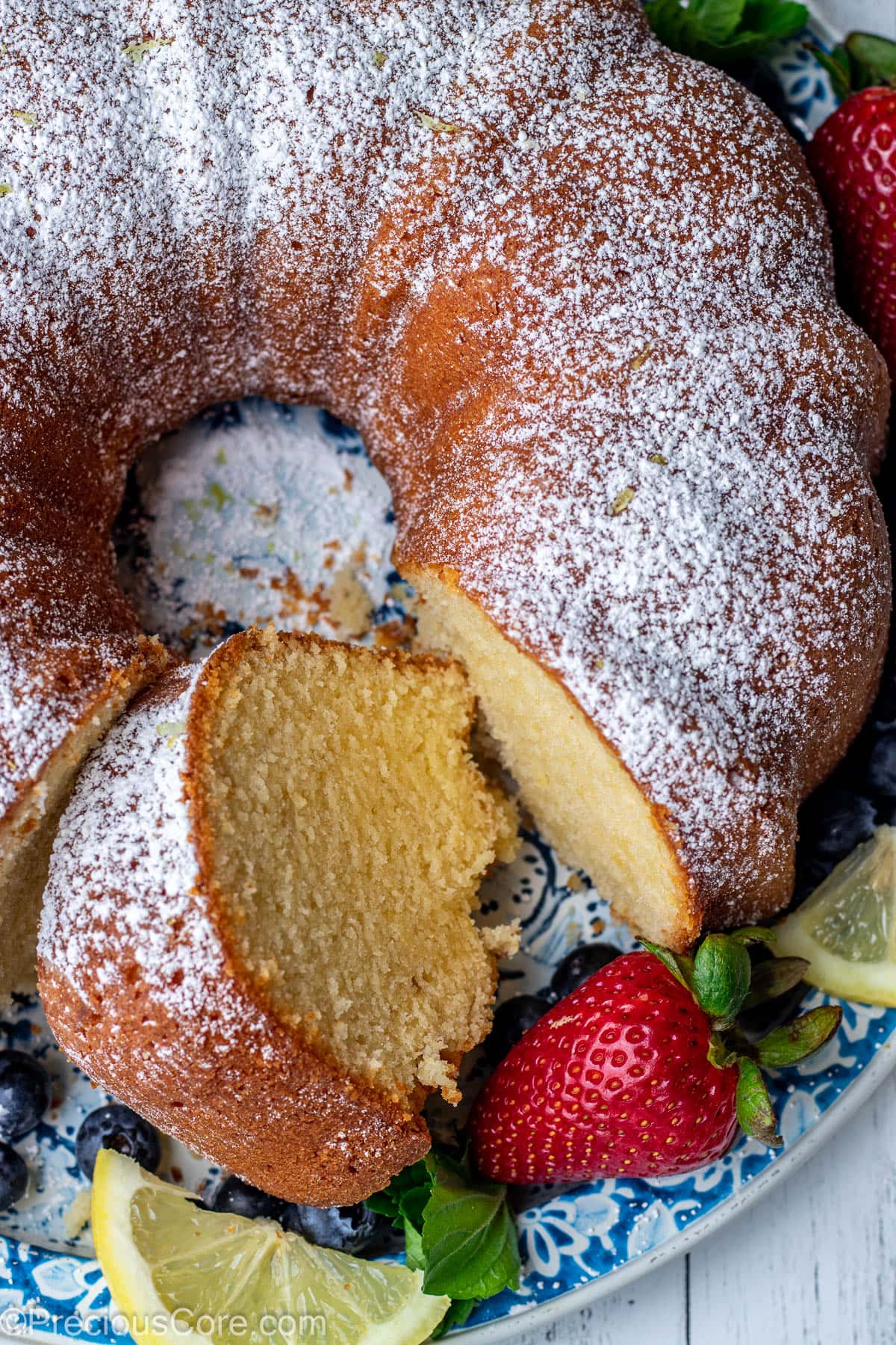 Lemon pound cake on a round platter with a piece of cake cut out.