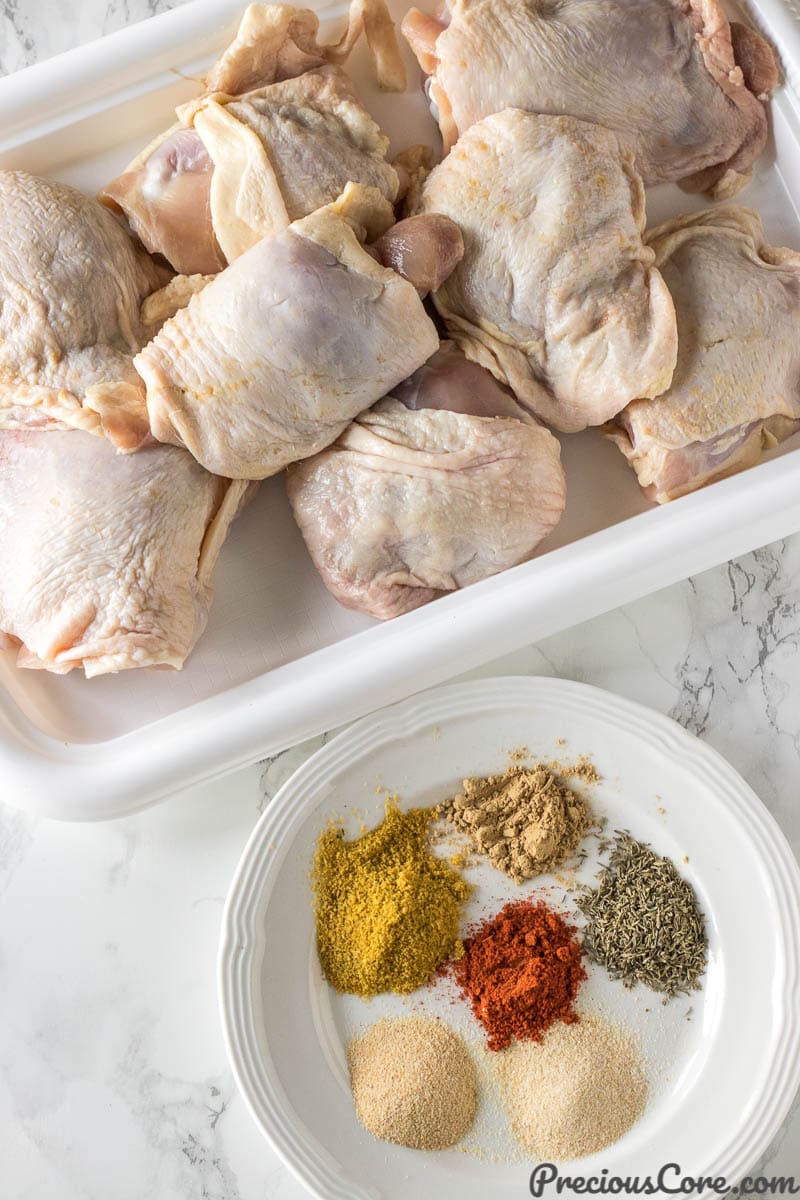 Dry rub ingredients on a plate and raw chicken thighs on a tray