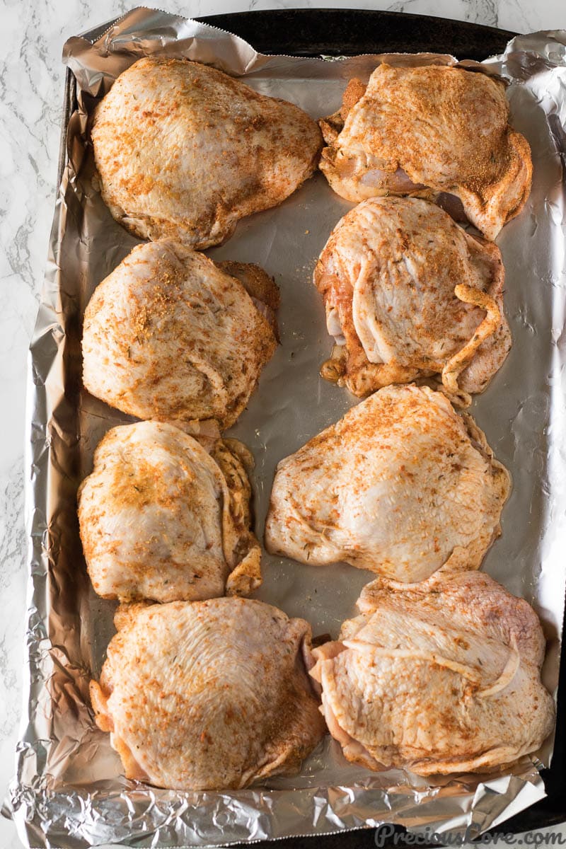 chicken thighs in a baking sheet with spices rubbed all over them