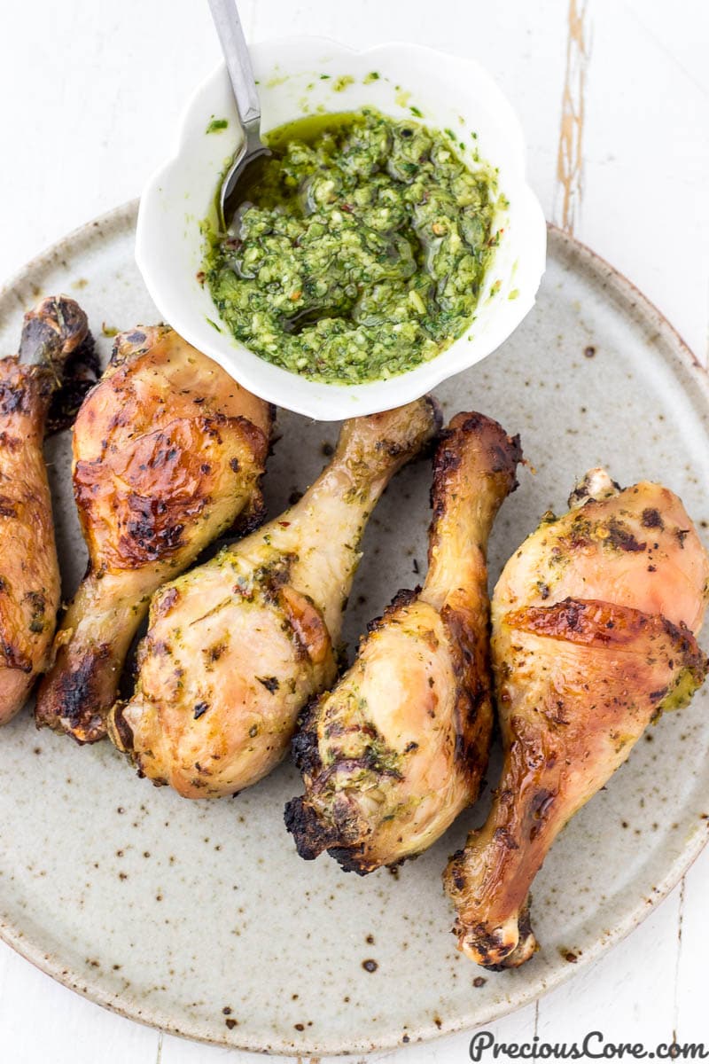 Grilled chicken on a plate with a bowl of green sauce nearby
