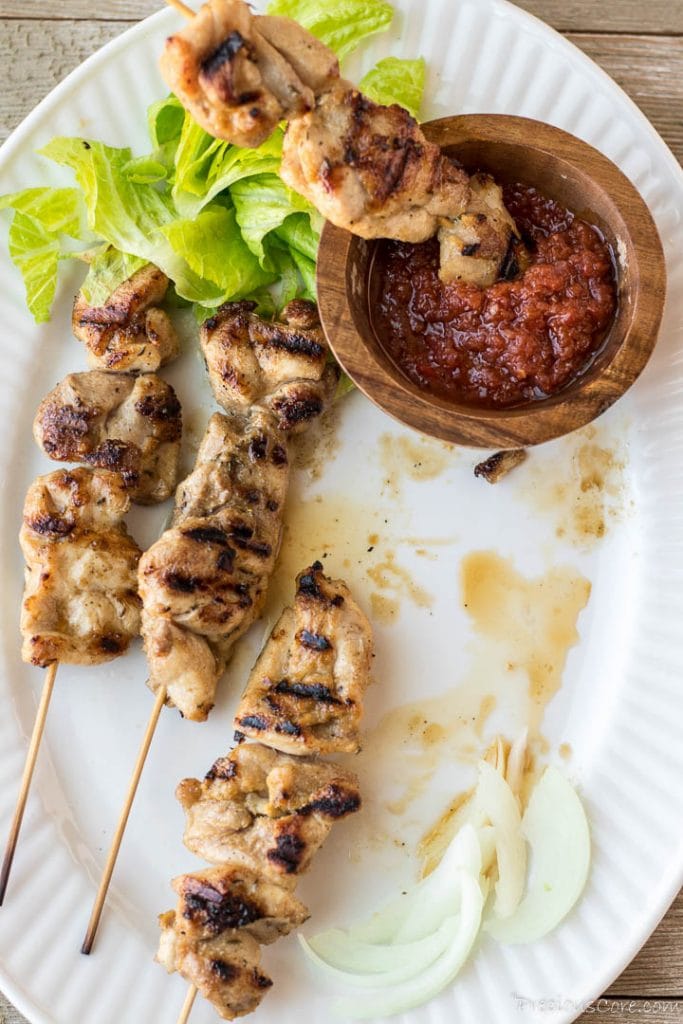 Chicken skewers with a wooden bowl of hot sauce and some vegetables