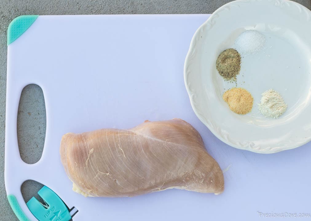 Chicken on cutting board, seasonings on plate