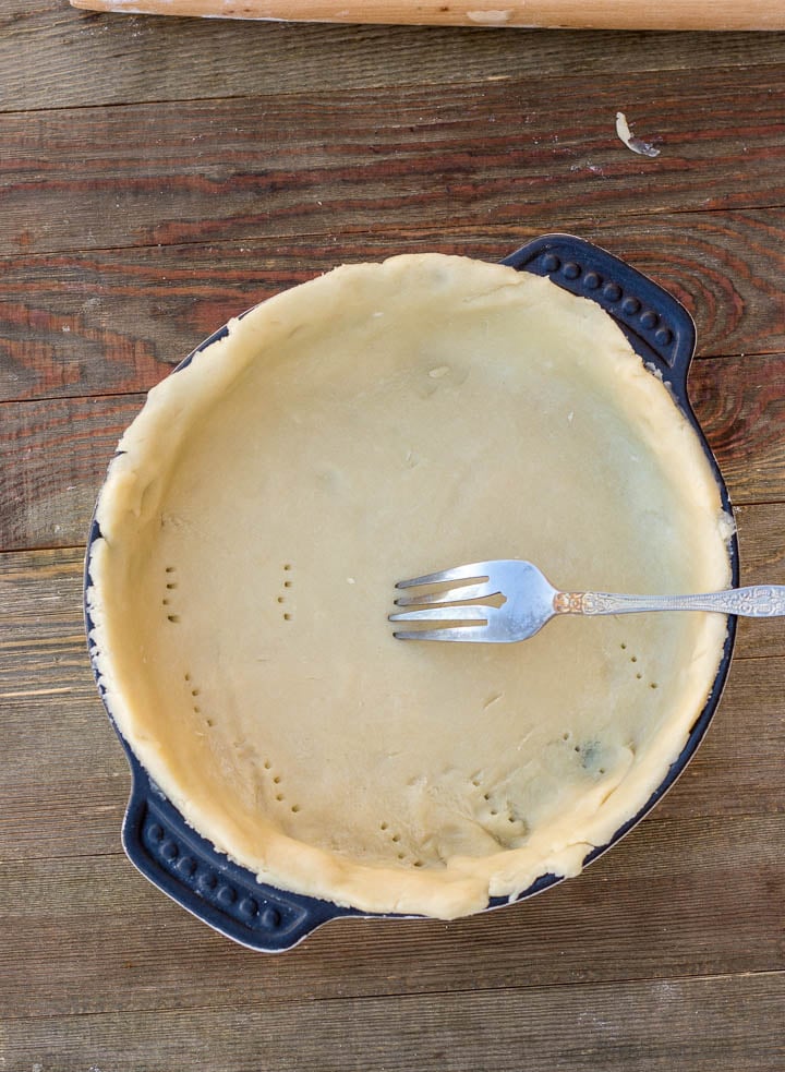 All butter crust in baking pan with a fork pricking the crust
