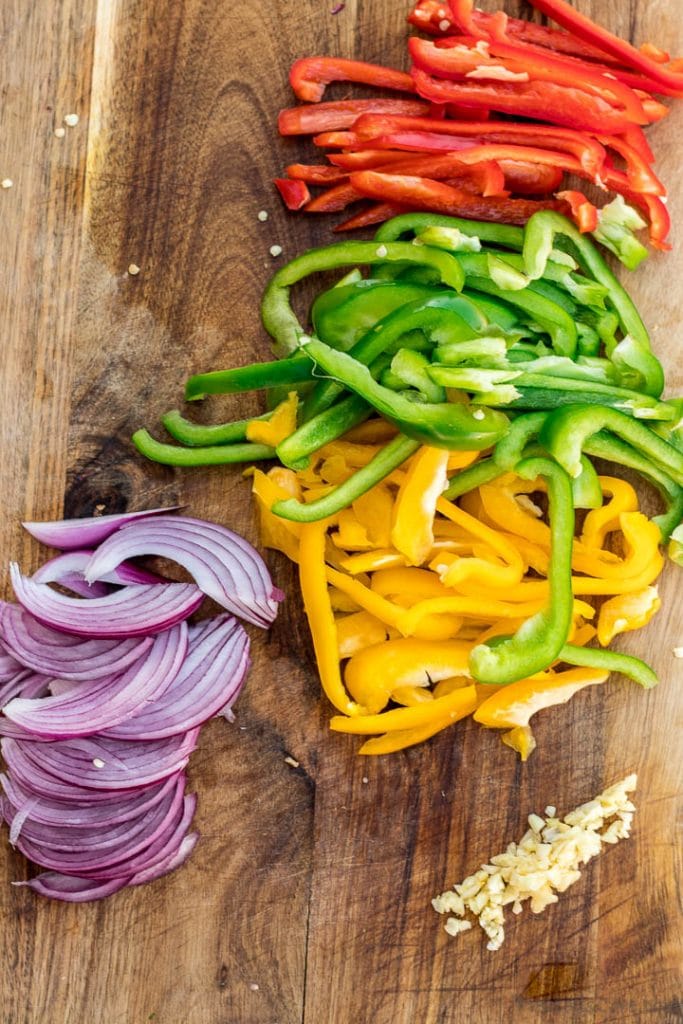 Sliced red, yellow and green bell pepper on a chopping board plus minced garlic