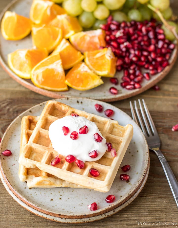 2 waffles on a plate with whipped cream and pomegranate seeds on top