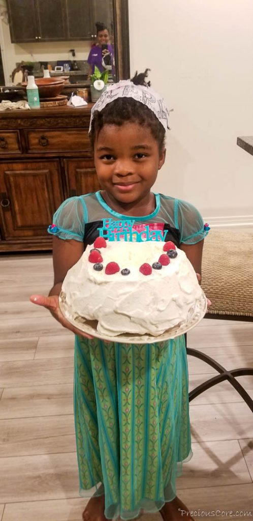 Girl wearing an Anna dress holding a cake that says \"Happy Birthday.\"