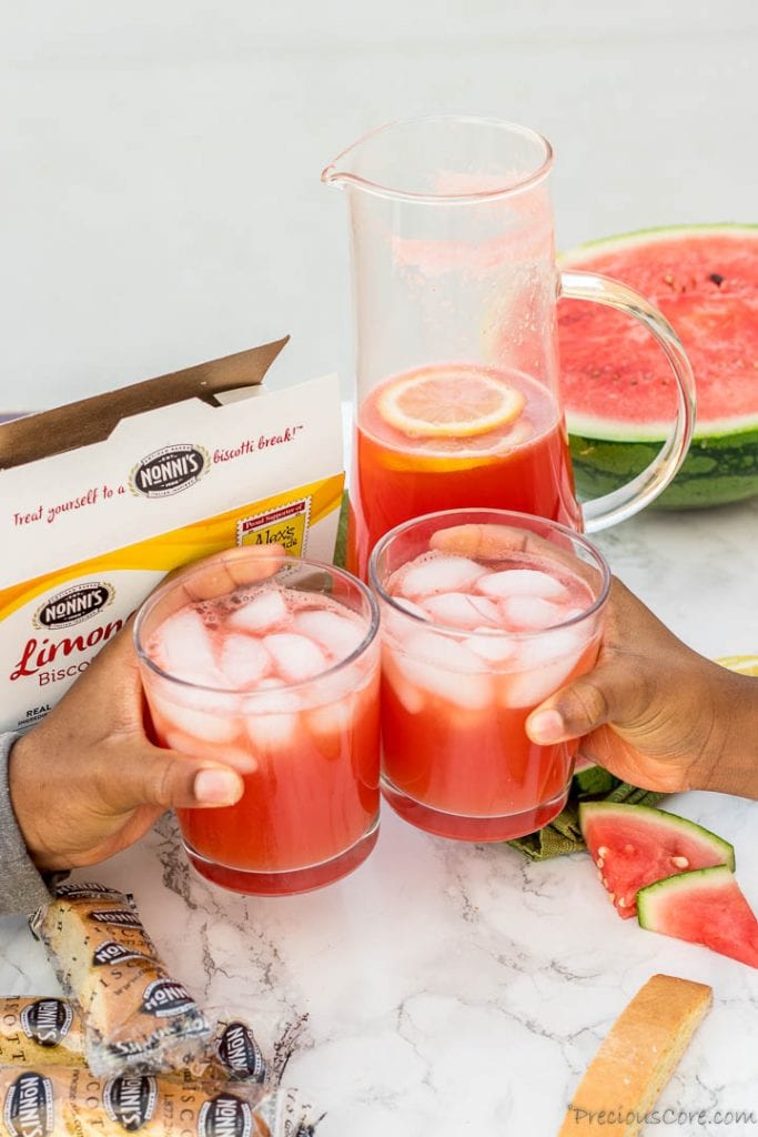 Two hands holding cups of fresh watermelon lemonade