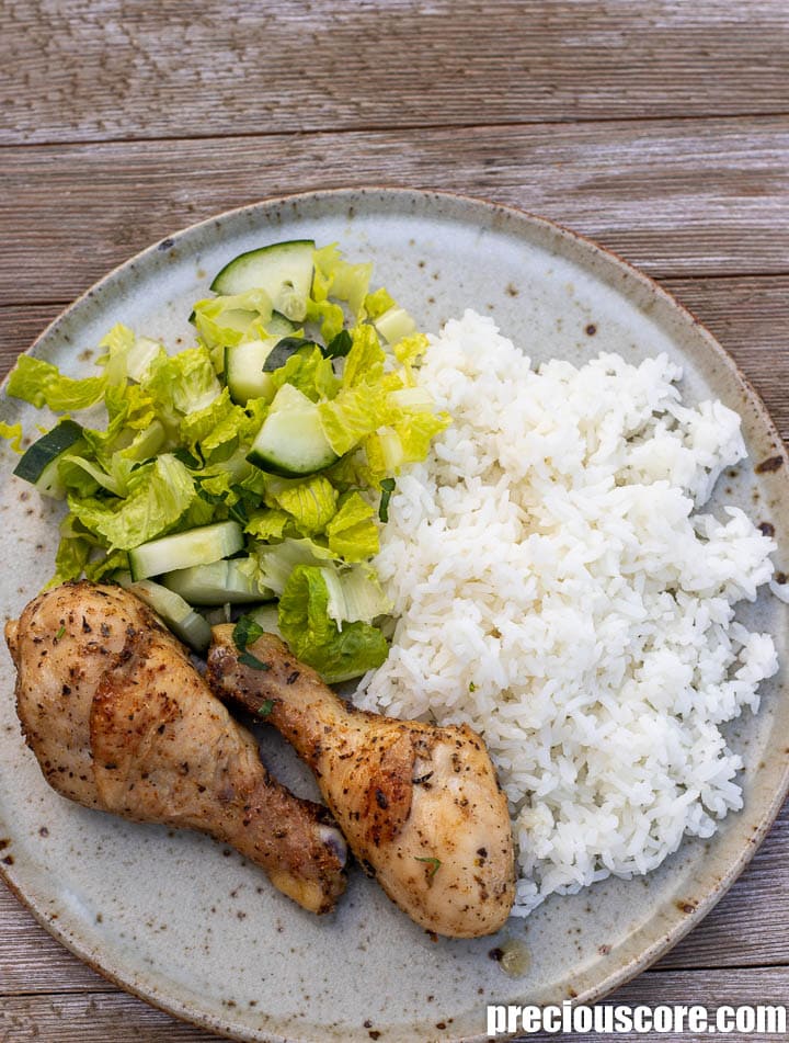 Chicken drumsticks, rice and lettuce on a plate.