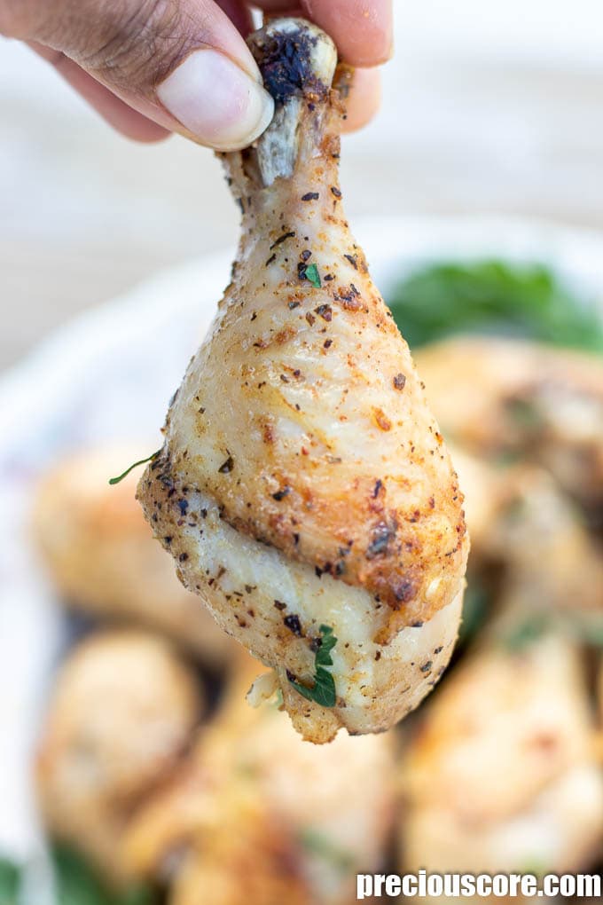 Hand holding a golden baked chicken drumstick.