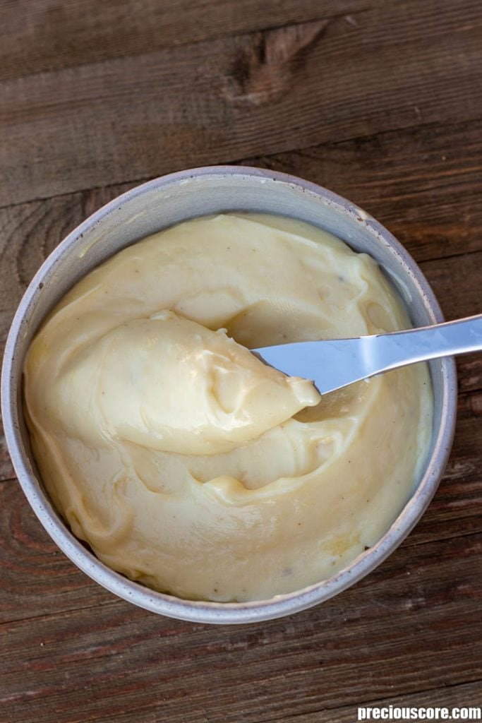 A bowl of freshly made mayonnaise, a butter knife lifting up some mayonnaise.