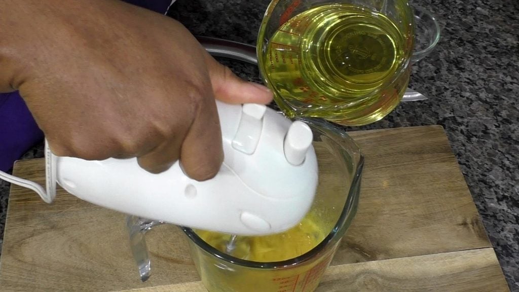 Hand holding hand mixer, another hand drizzling in oil to make mayonnaise