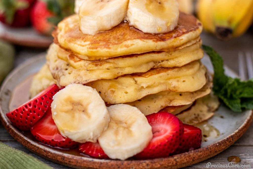 Pancakes on a plate topped with sliced bananas and strawberries