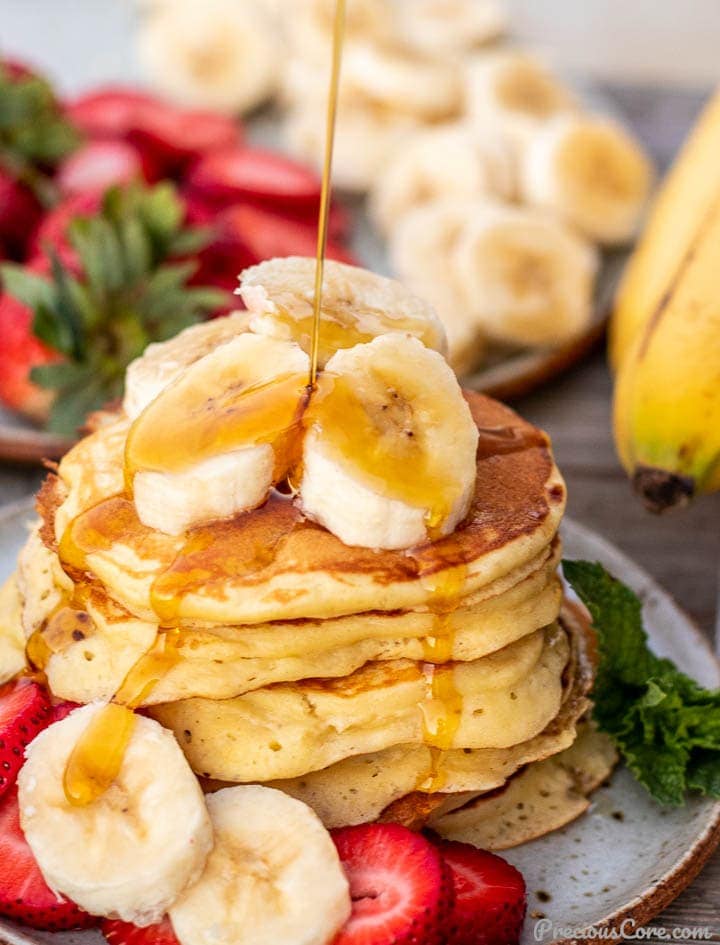 Stack of banana slices on a plate, banan slices on the stack and maple syrup pouring on top