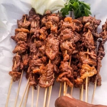 Hand grabbing a stic of beef soya from a platter of beef soya