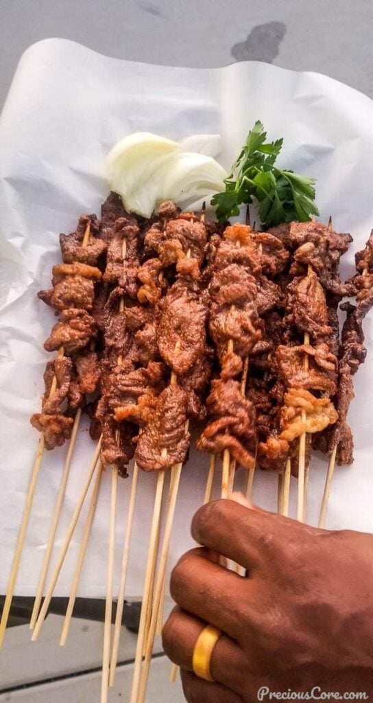 Hand grabbing a stic of beef soya from a platter of beef soya