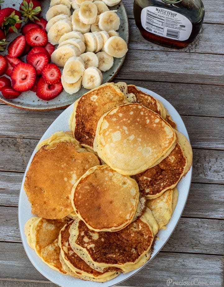 Platter of pancakes, plate of sliced bananas and strawberries on the side