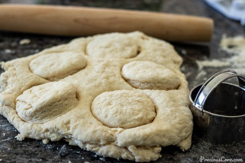 biscuit dough on counter top cut into circles, biscuit cutter on the side of dough