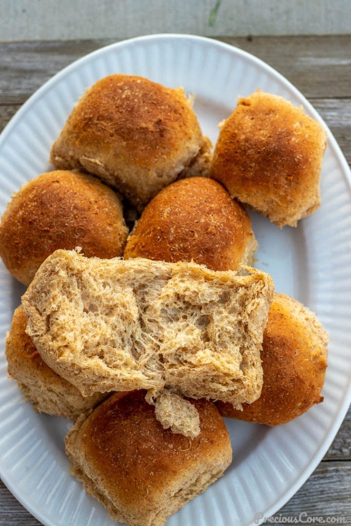 honey wheat rolls on a platter with one roll opened to show soft texture of the bread
