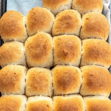 Baked honey whole wheat dinner rolls on a baking sheet lined with parchment paper