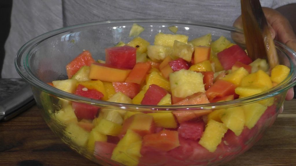fruit salad in a large mixing bowl, hand mixing salad with a wooden spoon